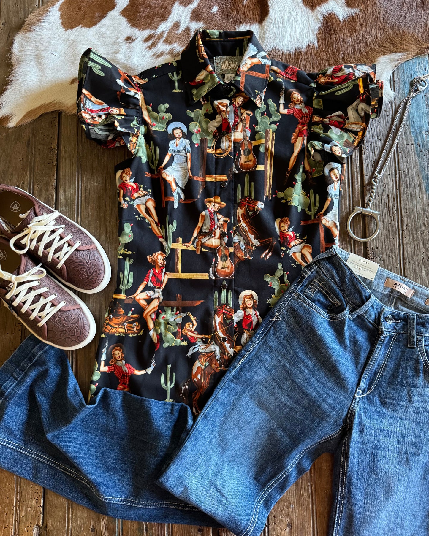 Blake Shirt (Cowgirl Pinup in Black) with jeans, shoes, and necklace on rustic wood background