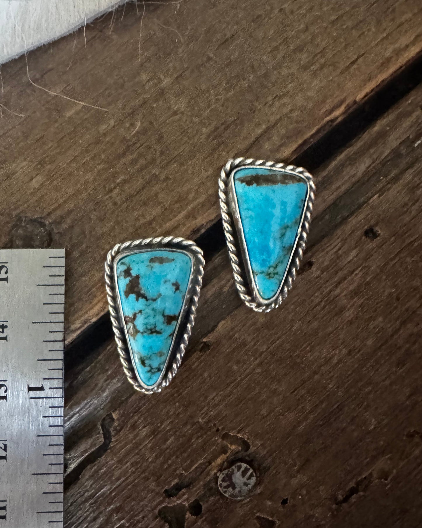 Turquoise earrings on a wooden surface with a ruler for scale.
