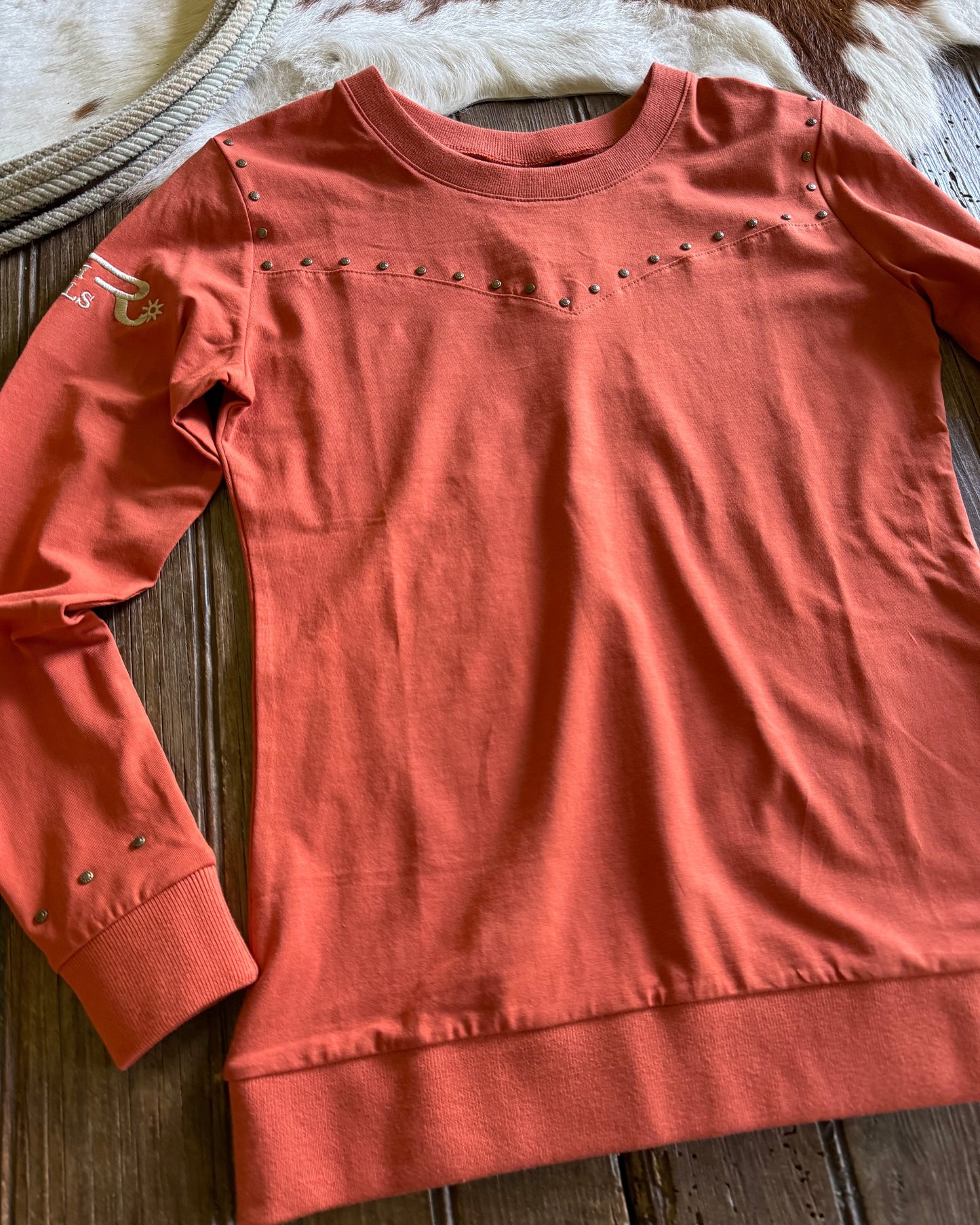 Coral-colored long-sleeve shirt with decorative elements on a wooden surface