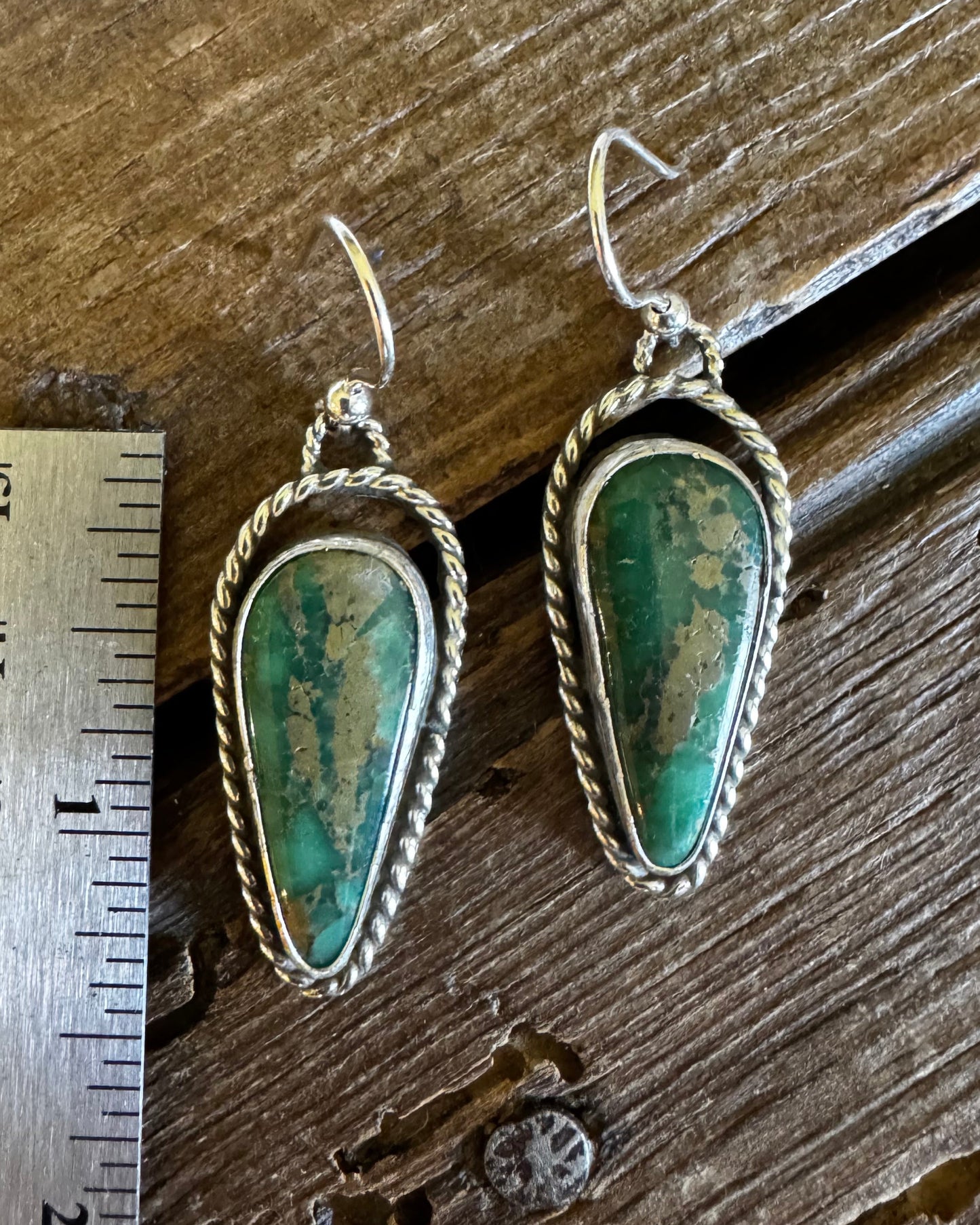 Pair of turquoise earrings on a wooden surface with a ruler for scale.