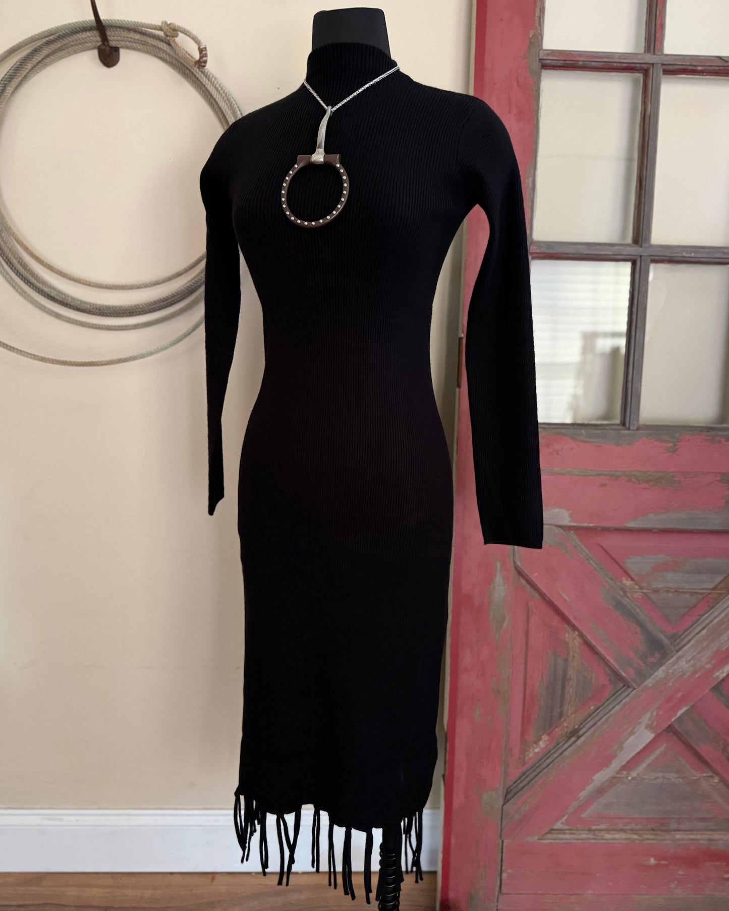 black sweater dress with fringe in front of a white wall with a rope and old door