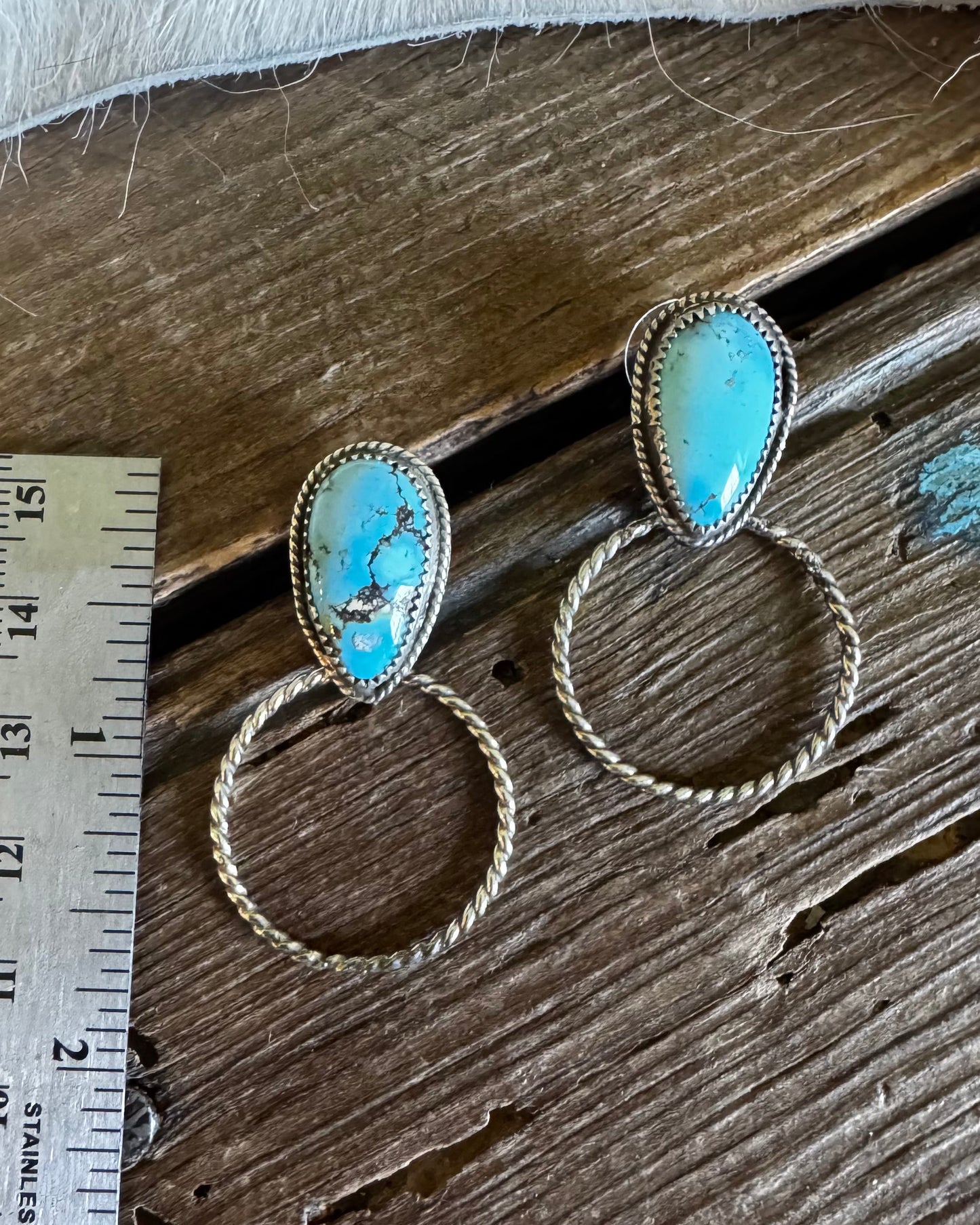 Turquoise stone earrings on a wooden surface with a ruler for scale.