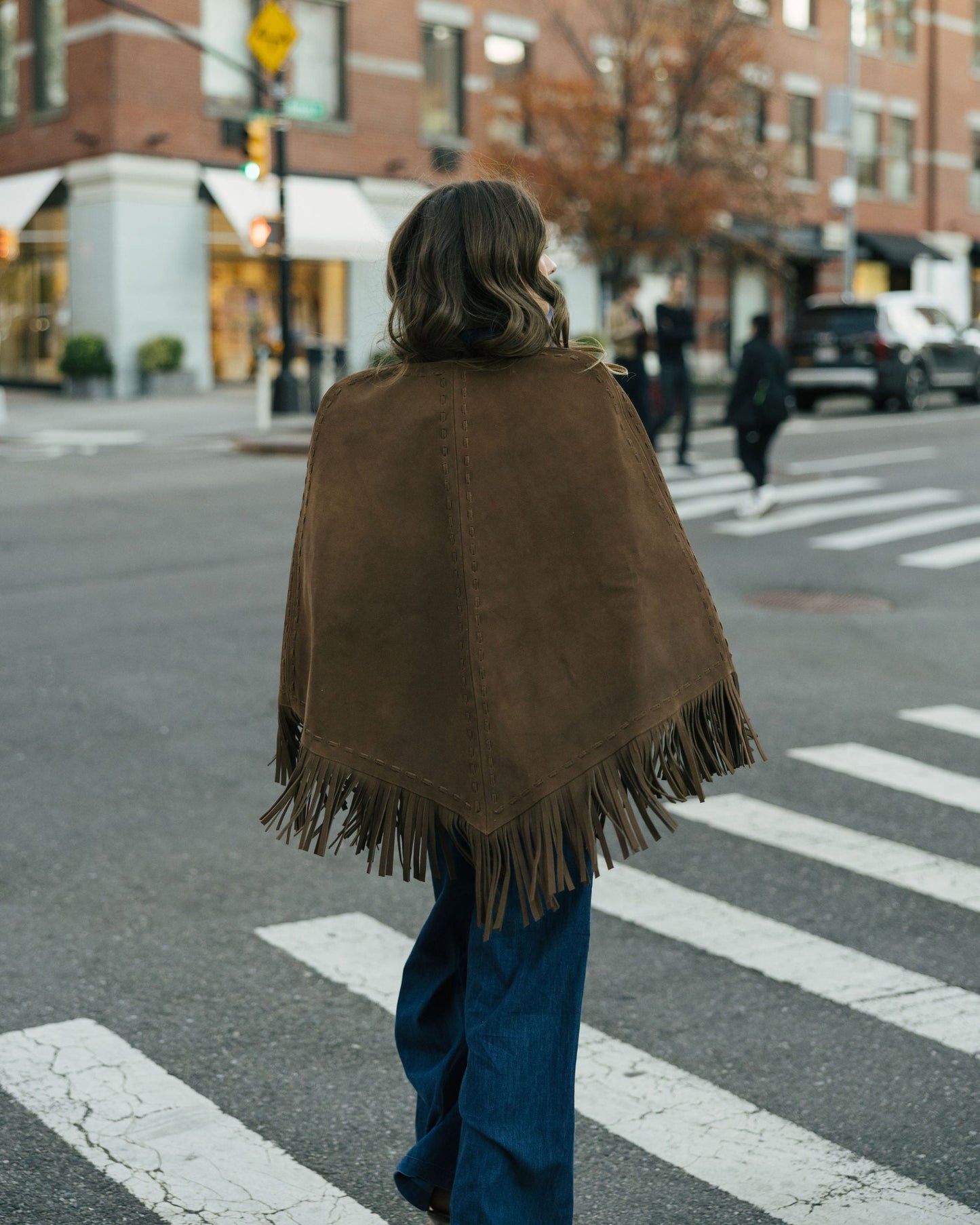Person wearing a brown fringed cape walking on a city street.