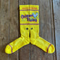 Cactus Alley Chicken Roping Performance Socks in yellow showing design on rustic wood background 
