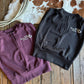 Black and purple shirts with 'Ranch Girl' branding on a wooden surface with cowhide rug.