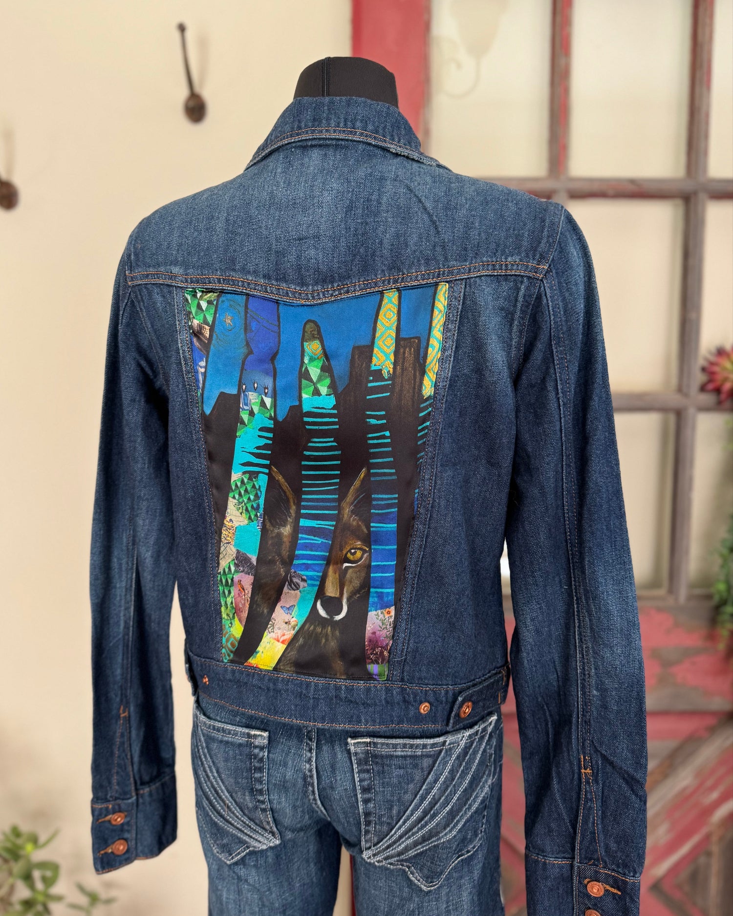 Denim jacket with colorful back design on a mannequin against a neutral background