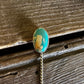 Pin with a green and gold design on a wooden surface