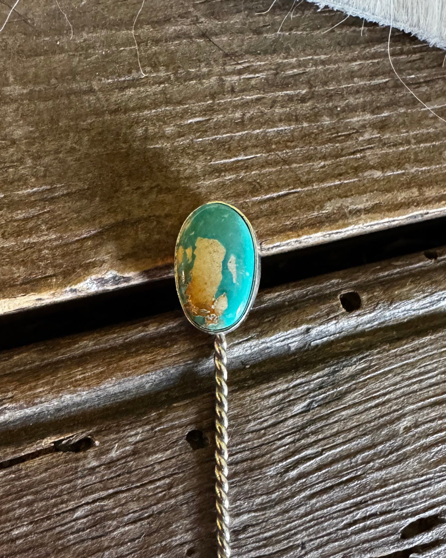 Pin with a green and gold design on a wooden surface