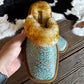 hand holding a turquoise embossed leather slipper above a wooden and cowhide background