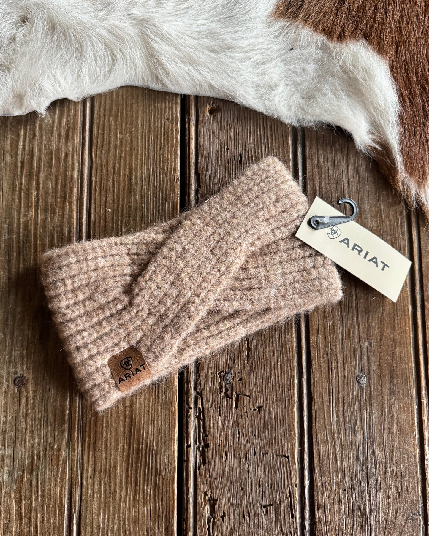 Beige knitted headband with Ariat tag on a wooden surface