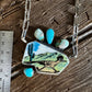 Necklace with a desert landscape pendant on a wooden surface next to a ruler for scale.