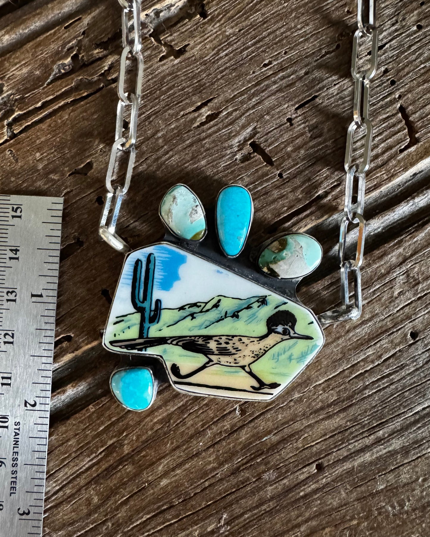 Necklace with a desert landscape pendant on a wooden surface next to a ruler for scale.