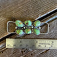 Jewelry pendant with green stones and silver accents on a wooden surface with a ruler for scale.