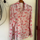 A long-sleeve button-up shirt with a pink and red horse pattern, hanging on a wooden hanger from a black wall hook.