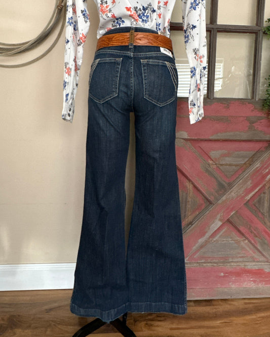 Dark blue jeans with a brown belt on a wooden floor.