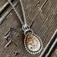 A silver chain necklace with a teardrop-shaped pendant featuring a brown and white marbled pattern, displayed on a rustic wooden surface.
