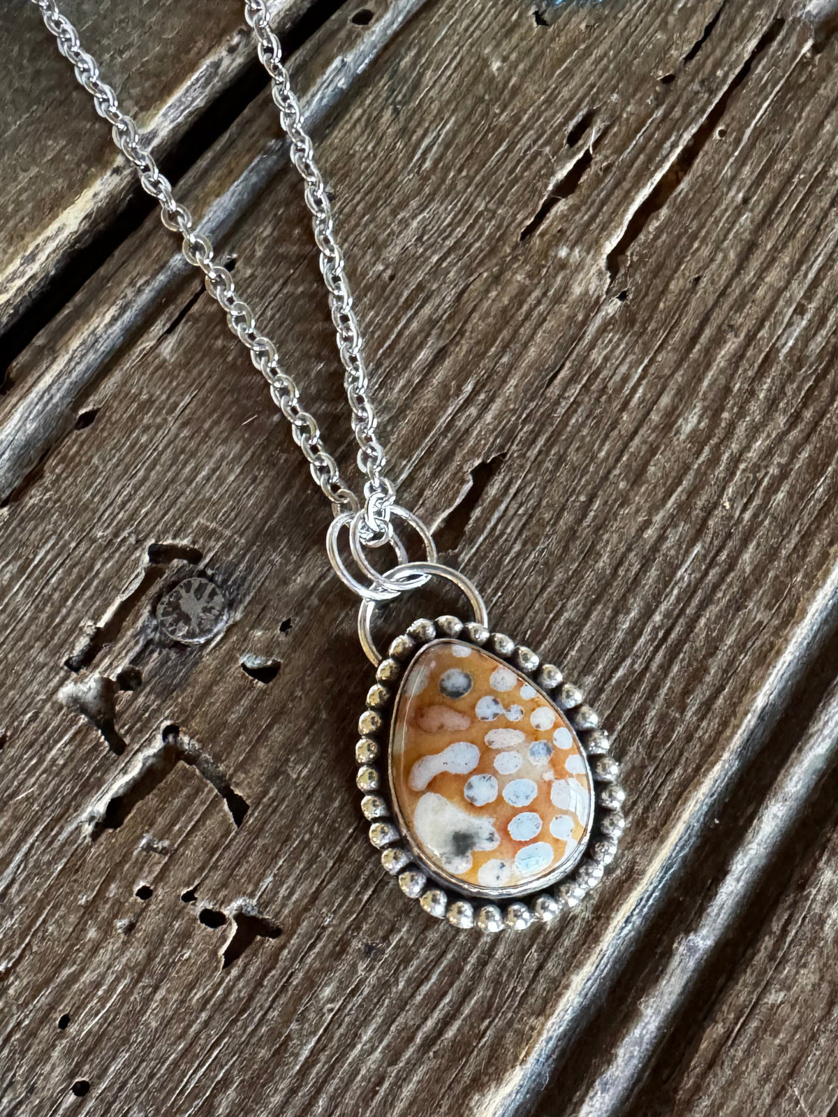 A silver chain necklace with a teardrop-shaped pendant featuring a brown and white marbled pattern, displayed on a rustic wooden surface.