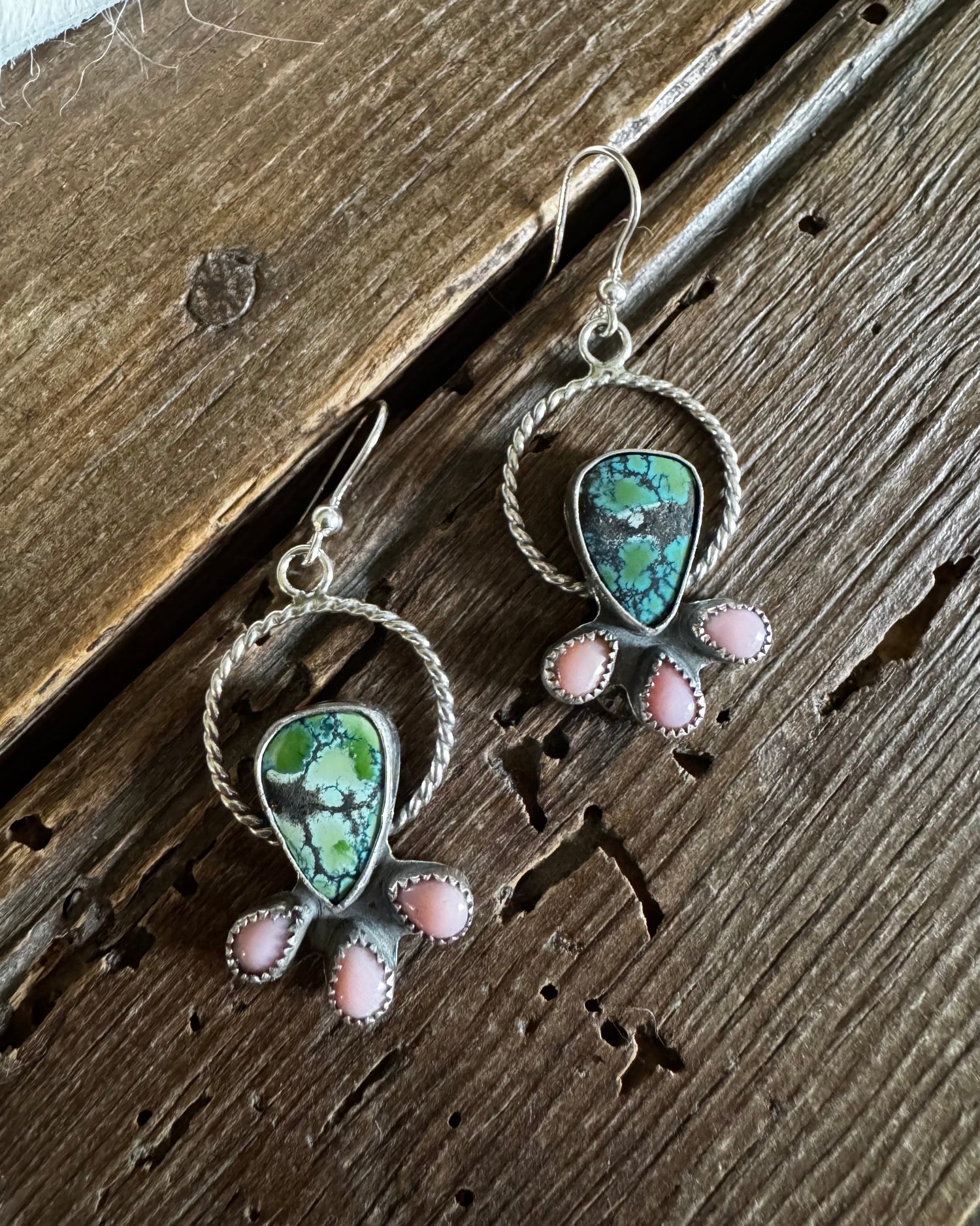 Silver earrings with green and pink stones on a wooden surface