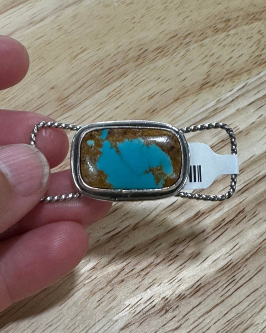 Turquoise stone pendant with silver frame held by a hand on a wooden surface