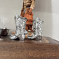 Silver cowboy boot-shaped objects on a wooden surface with a blurred background
