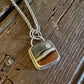 A silver-toned chain necklace with a square pendant featuring a marbled pattern of brown, beige, and gray, resting on a rustic dark wood surface.