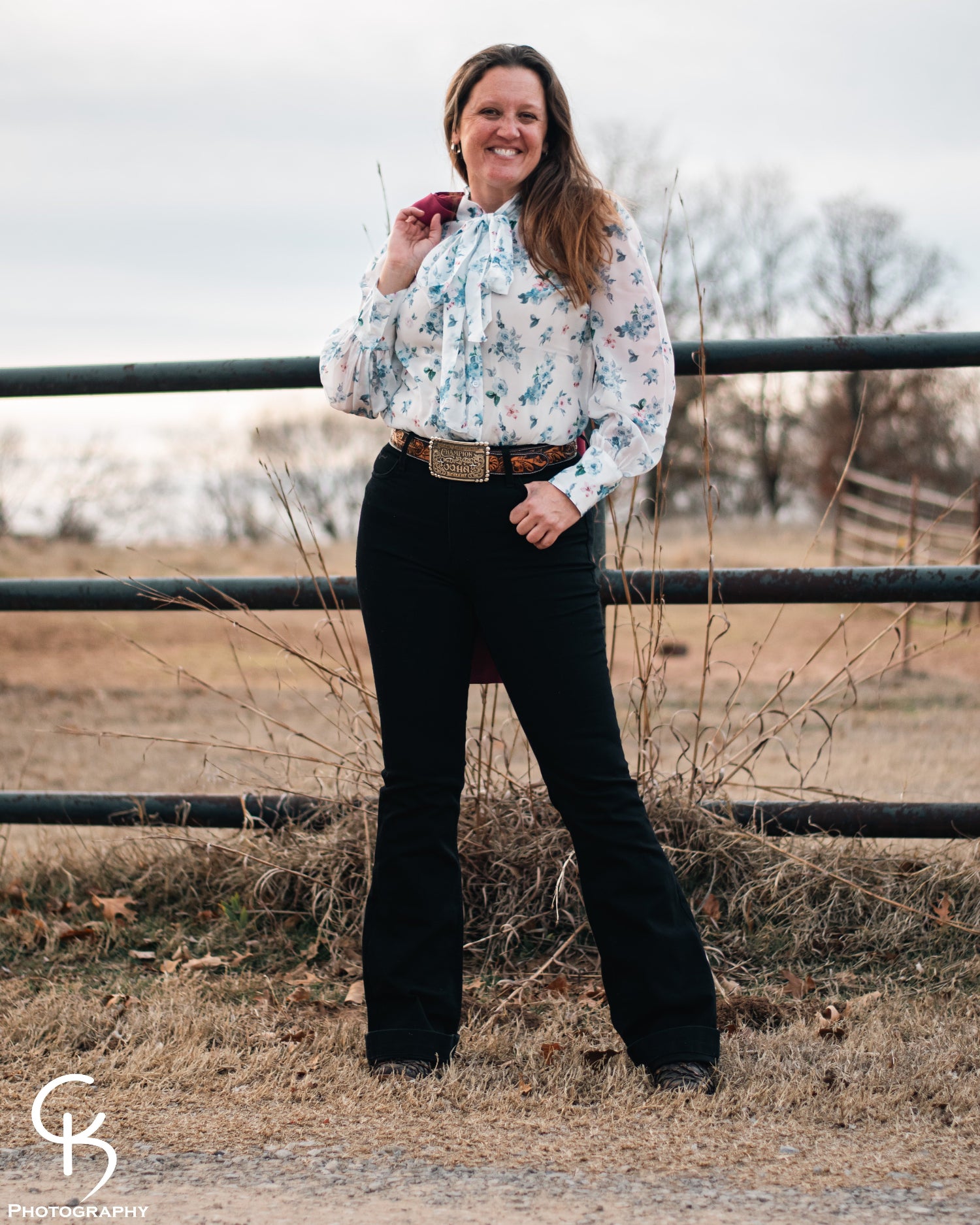 Model standing by a pipe fence in a field, dressed in a stylish modern western outfit.