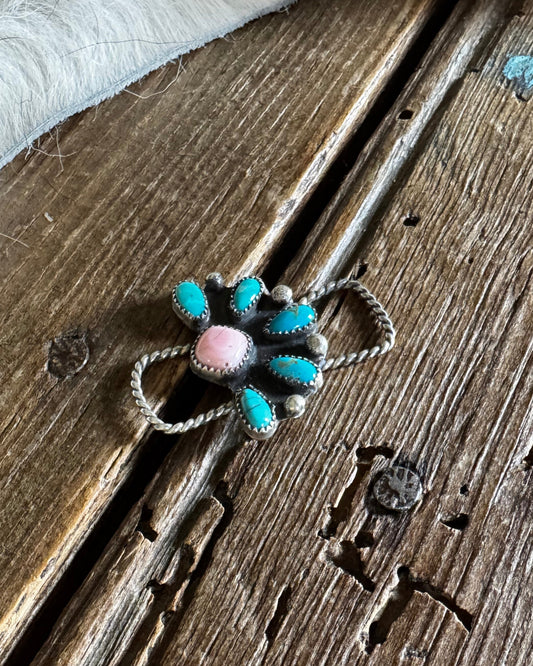 Silver flower-shaped twilly slide with turquoise and pink stones on a wooden surface