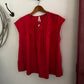 Red blouse on a wooden hanger against a white wall.