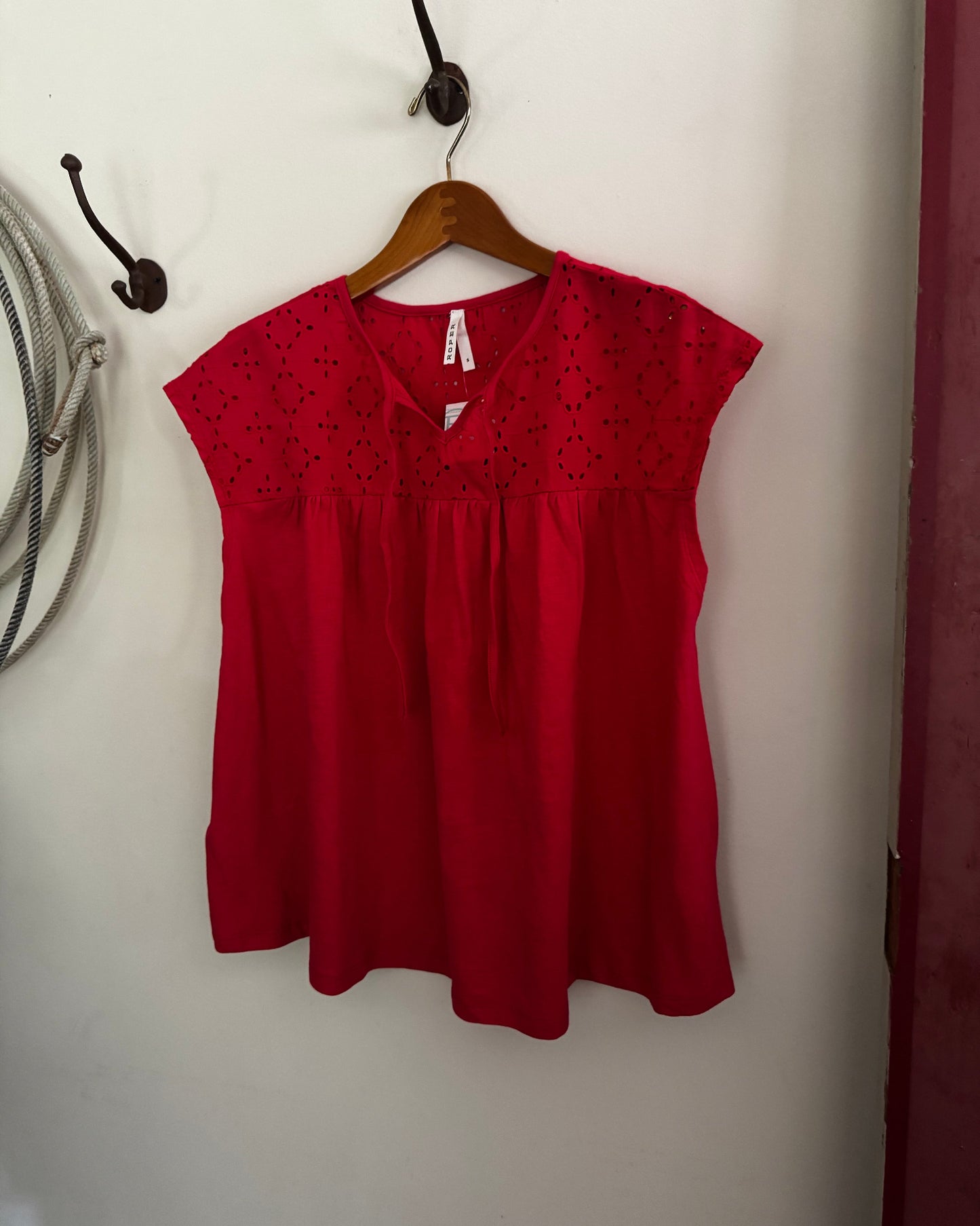Red blouse on a wooden hanger against a white wall.