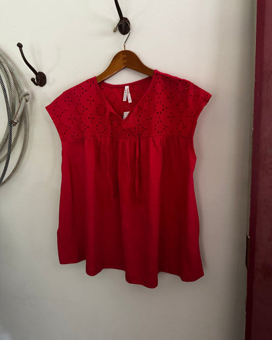 Red blouse on a wooden hanger against a white wall.