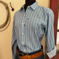 Person wearing a blue striped shirt and jeans with a belt, standing on a beige floor.