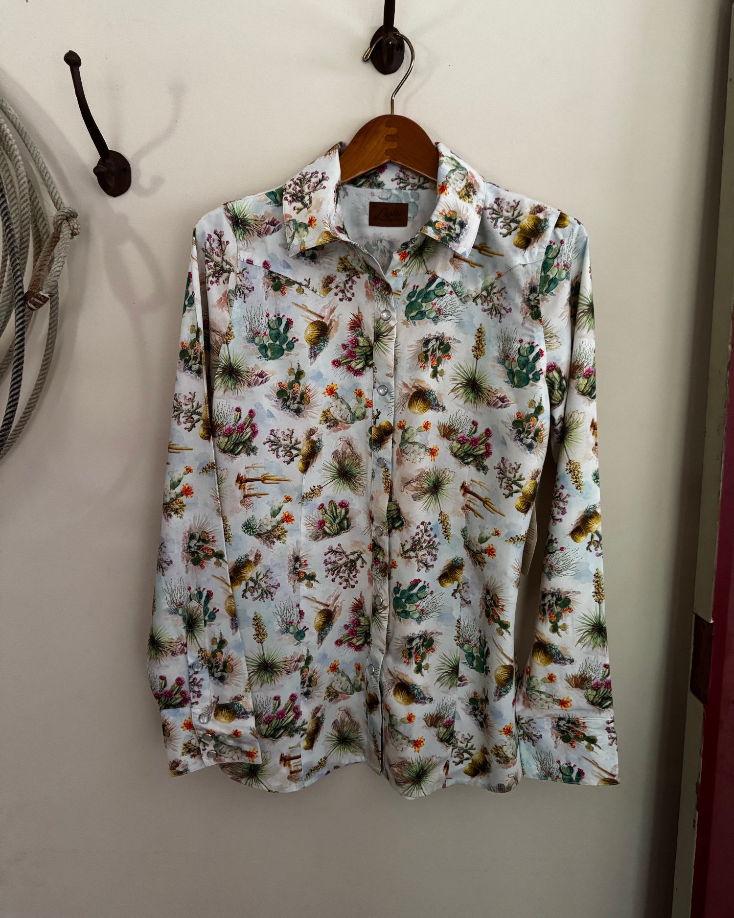 Floral patterned shirt hanging on a wooden hanger against a white wall.