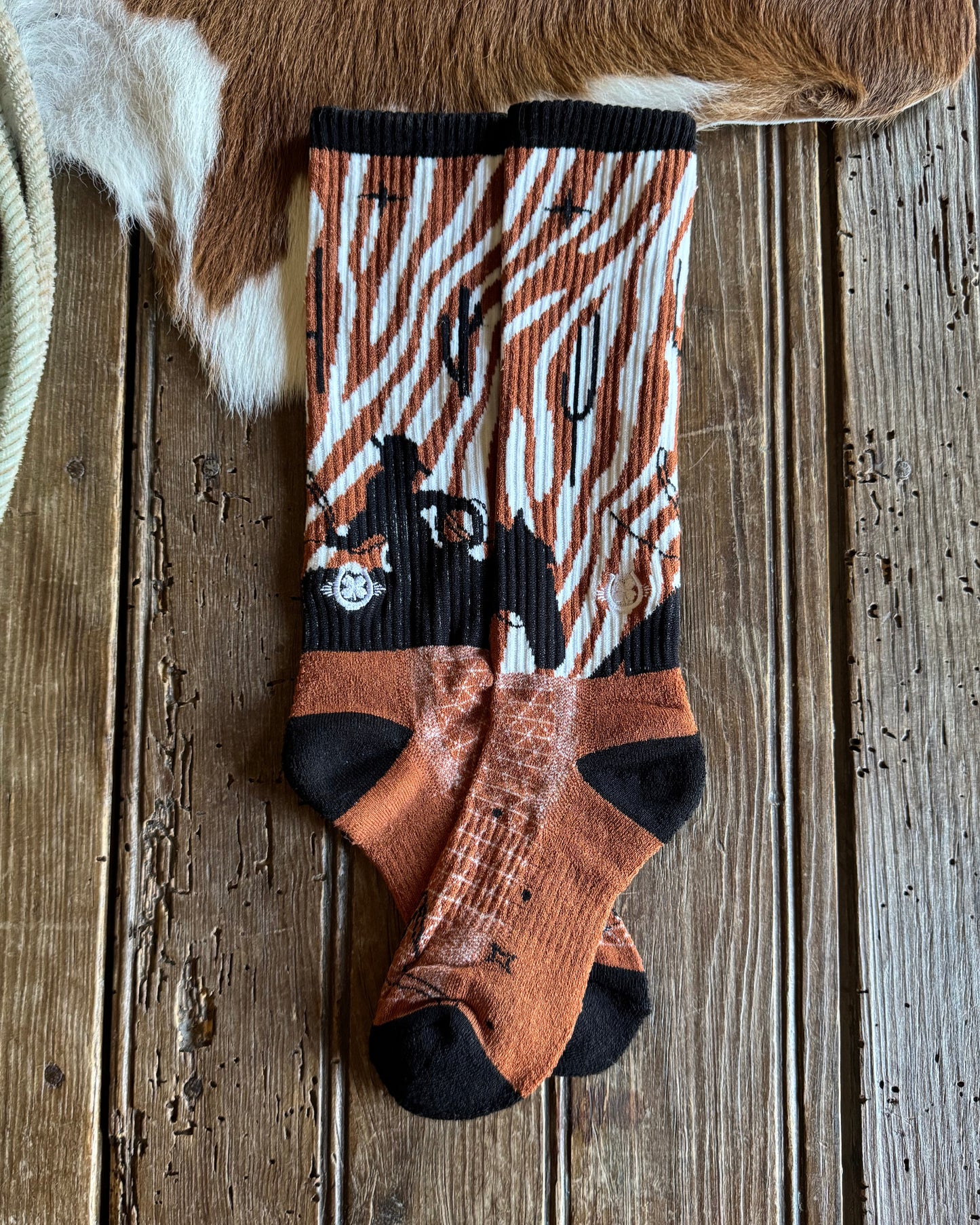 Pair of patterned socks on a wooden surface with a cowhide rug and rope.