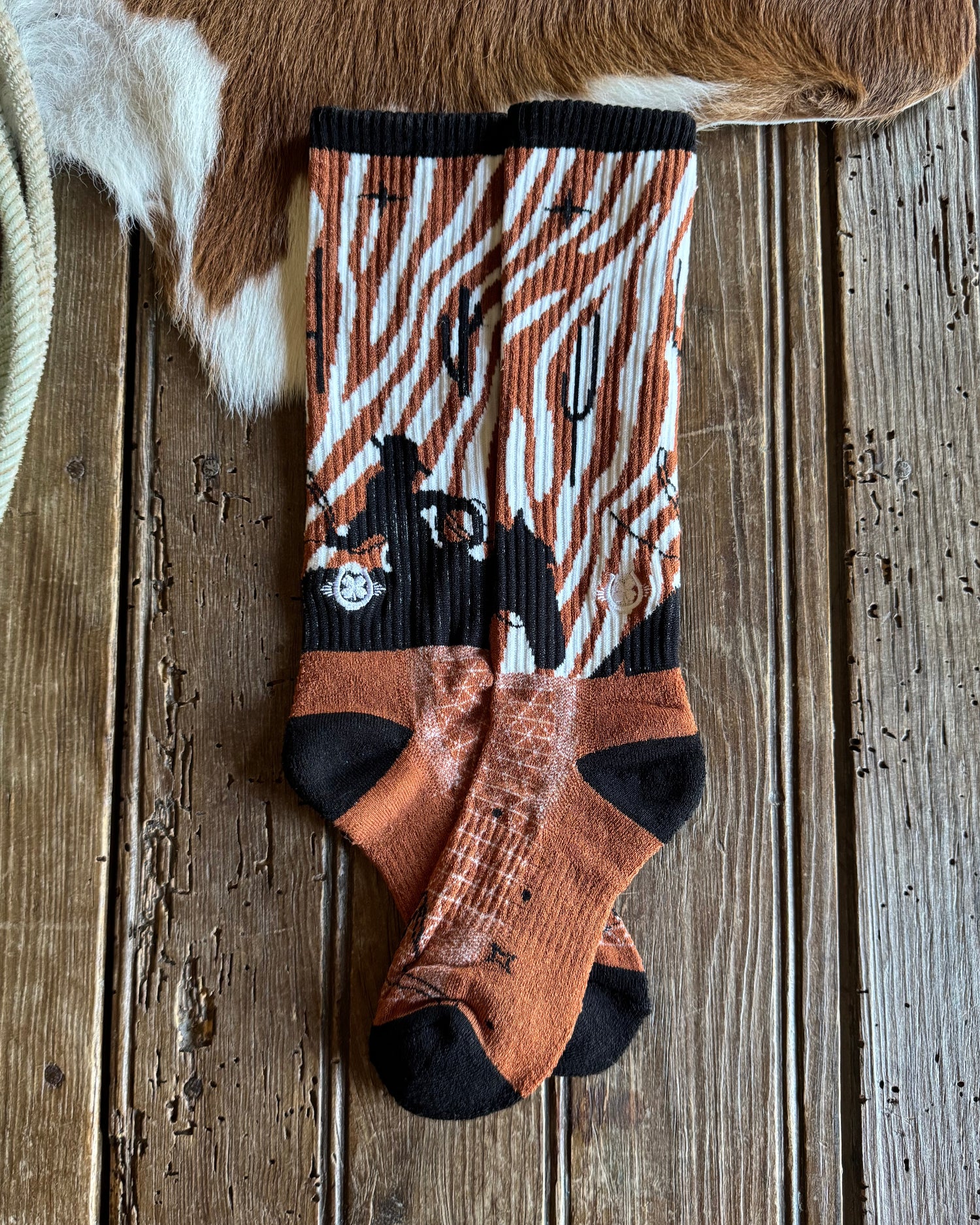 Pair of patterned socks on a wooden surface with a cowhide rug and rope.