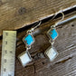 Pair of earrings with turquoise and beige stones on a wooden surface with a ruler for scale.