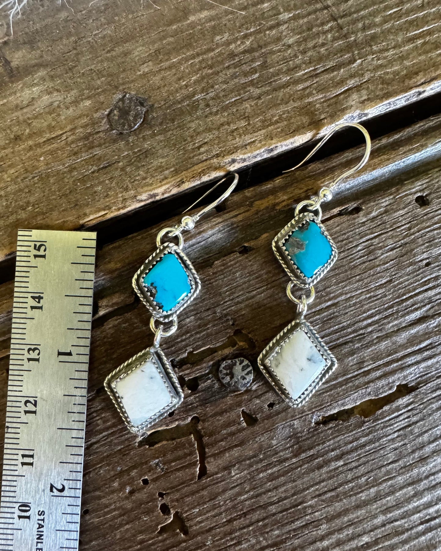 Pair of earrings with turquoise and beige stones on a wooden surface with a ruler for scale.