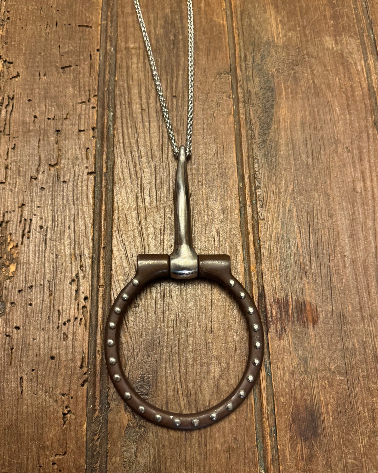 Metal snaffle bit with chain on a wooden surface