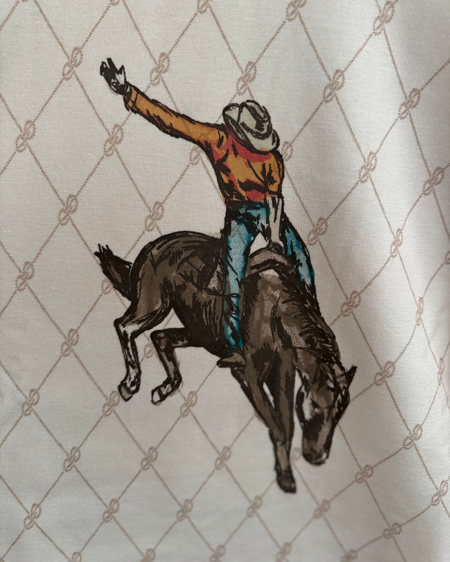 Embroidered design of a cowboy riding a bucking bronco on a textured fabric background
