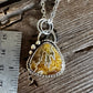 A silver pendant necklace with a triangular agate stone pendant, displayed next to a stainless steel ruler on a rustic wooden surface.