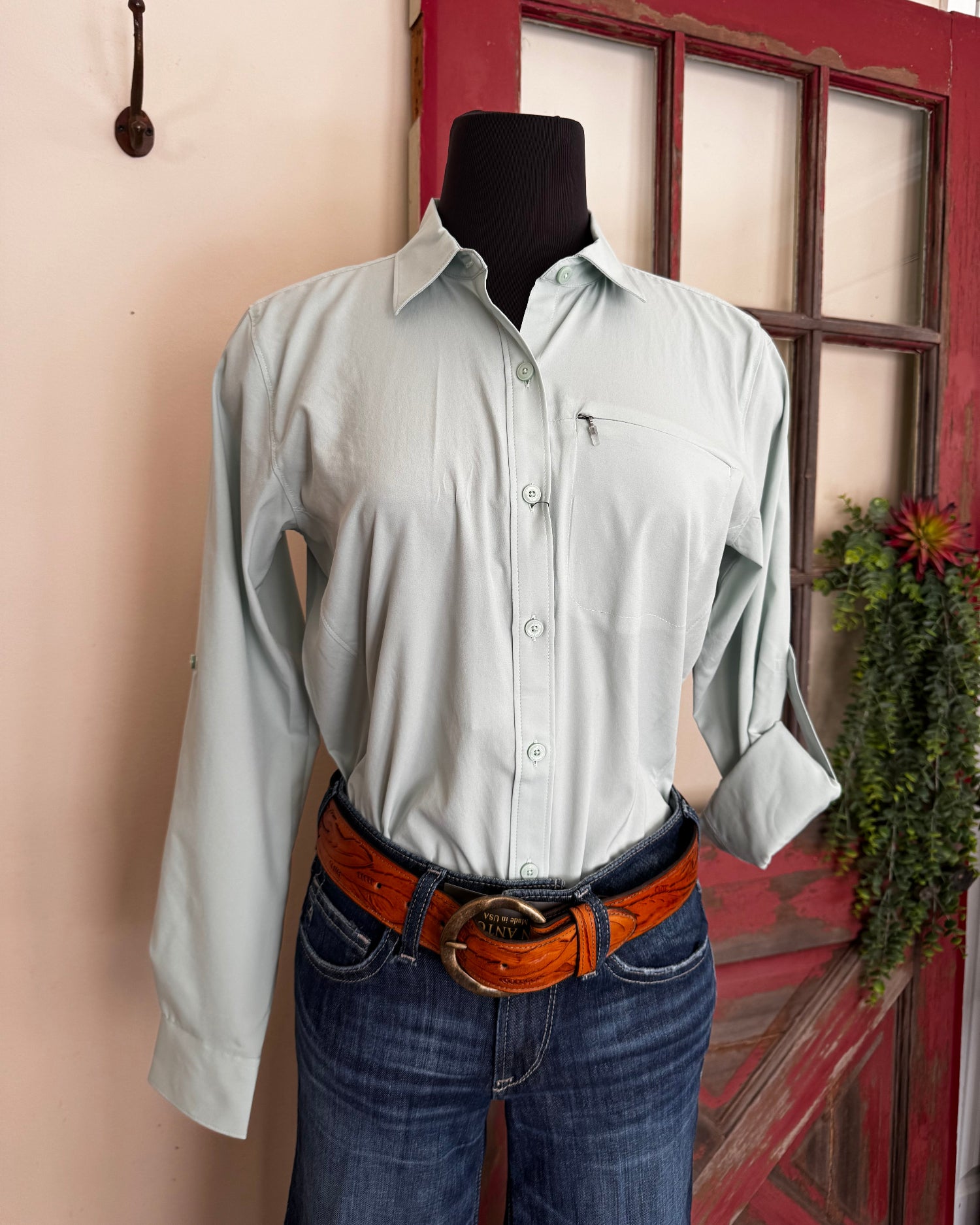Person wearing a light green shirt and blue jeans with a brown belt, standing in front of a red door.