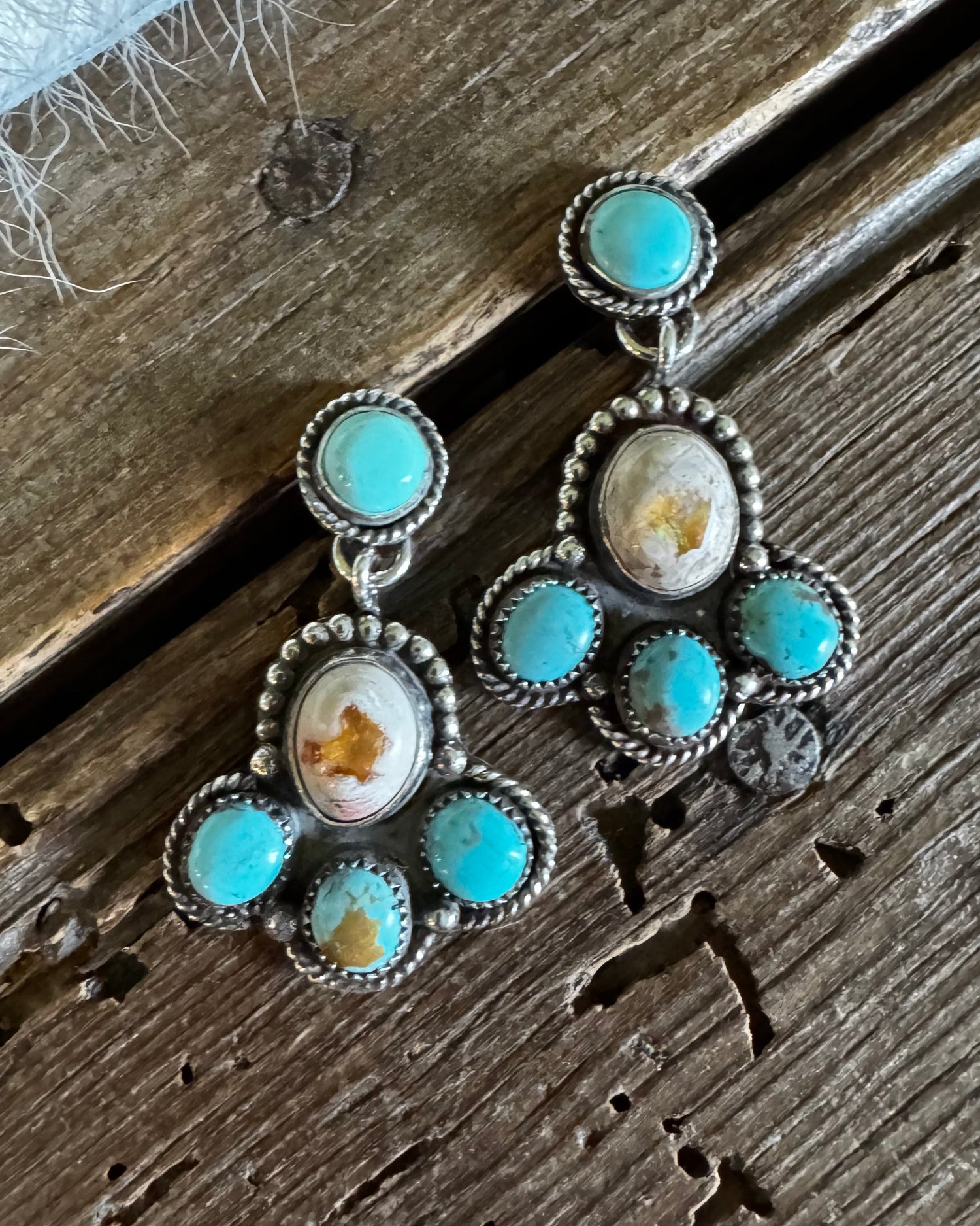 A pair of silver-toned dangle earrings with turquoise and natural stone accents, displayed on a rustic wooden surface.