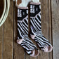 Pair of zebra-striped socks on a wooden surface with a cowhide rug in the background.