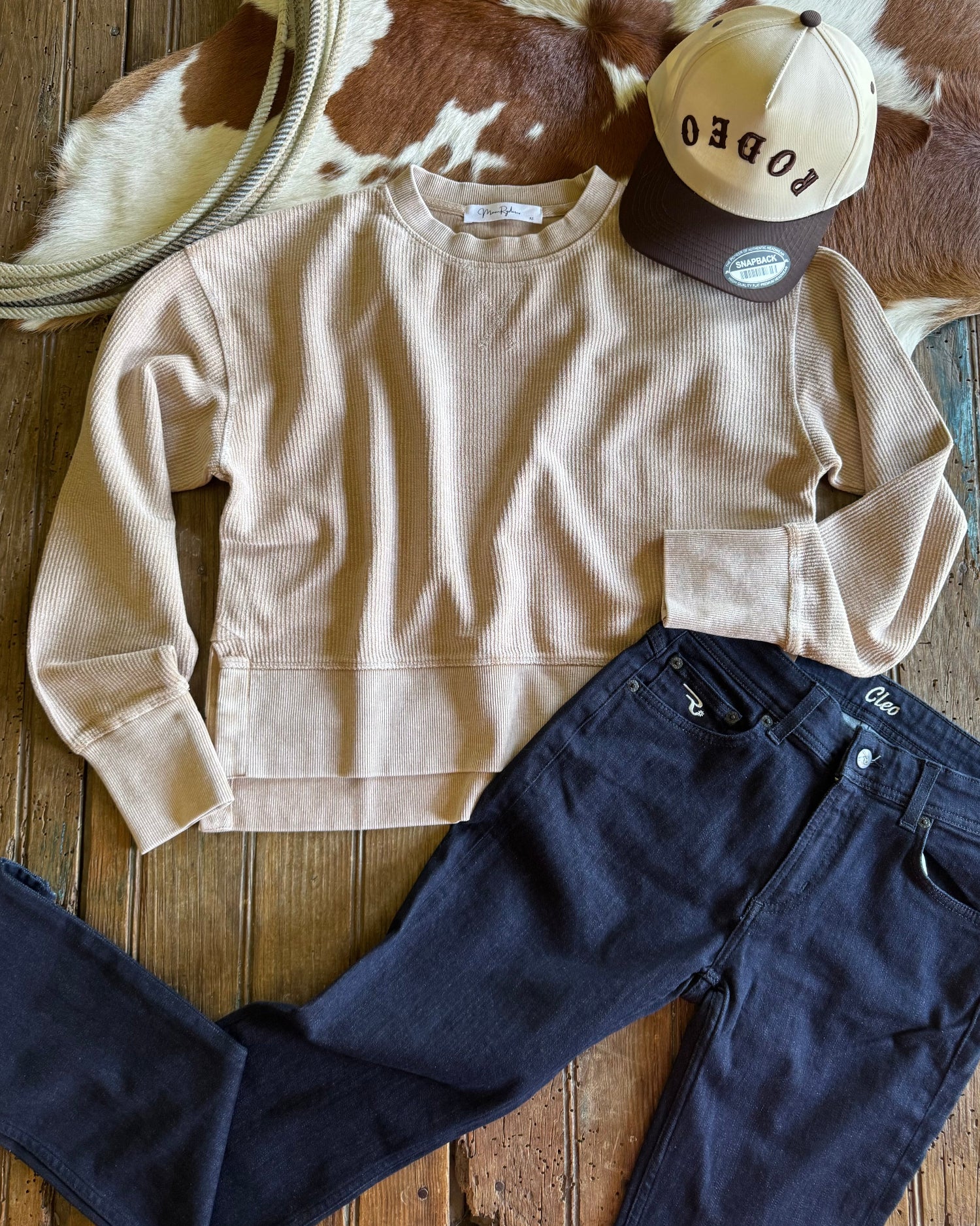 Beige sweatshirt, navy pants, and cap on a wooden surface with cowhide rug