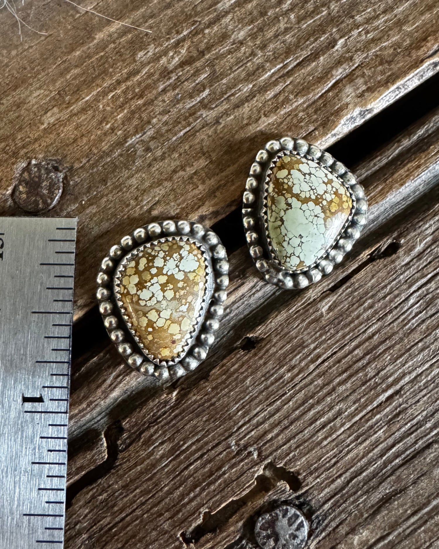 Pair of earrings on a wooden surface with a ruler for scale.