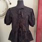 Black patterned blouse on a mannequin against a neutral wall.