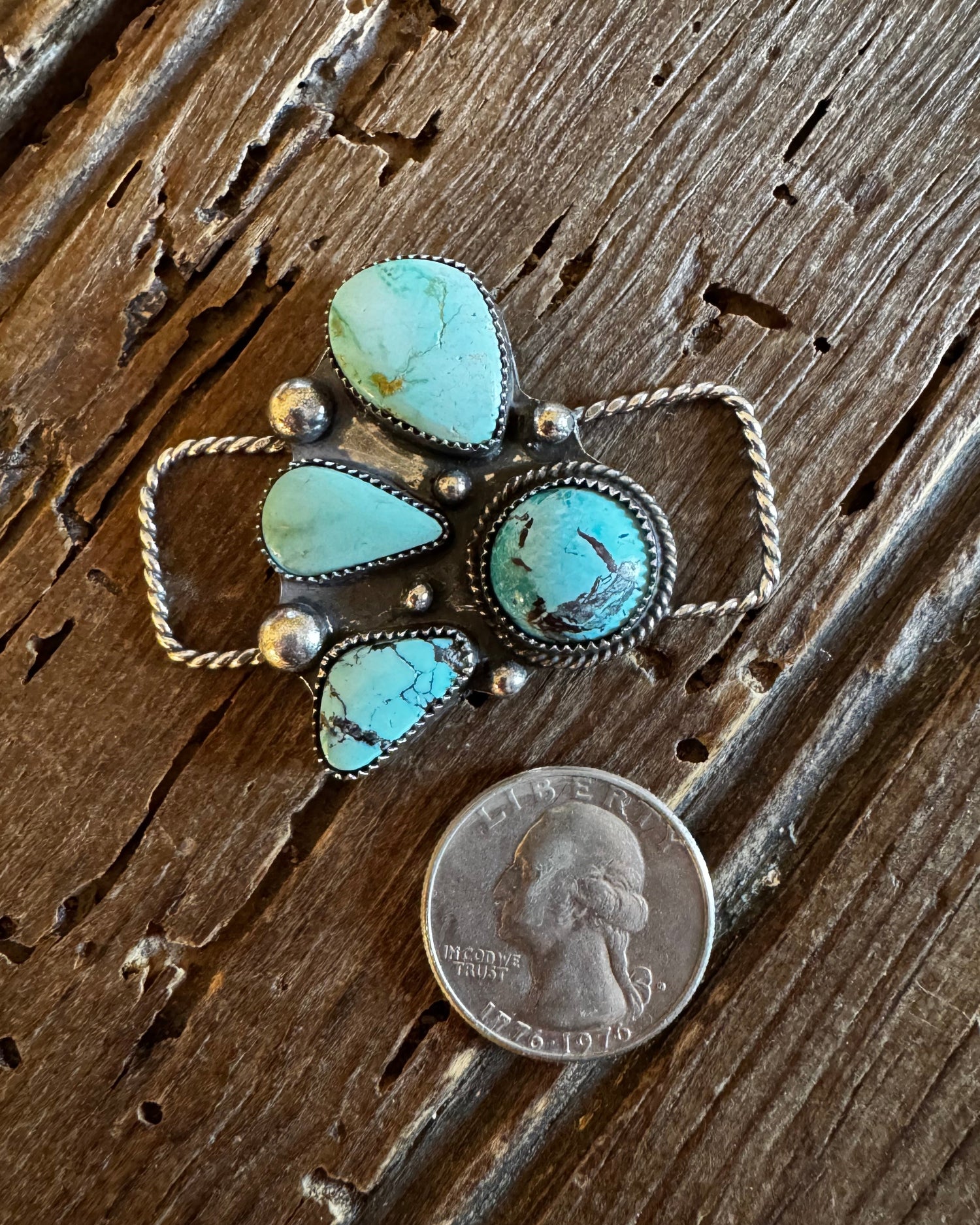 Turquoise pendant with silver accents next to a penny on a wooden surface