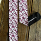 A pair of patterned knee-high socks and a black fabric drawstring bag on a rustic wooden surface. The socks have a white background with a dusty purple floral toile pattern and black cuffs and toes.