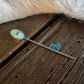 Teal stone hairpin on a wooden surface with fur