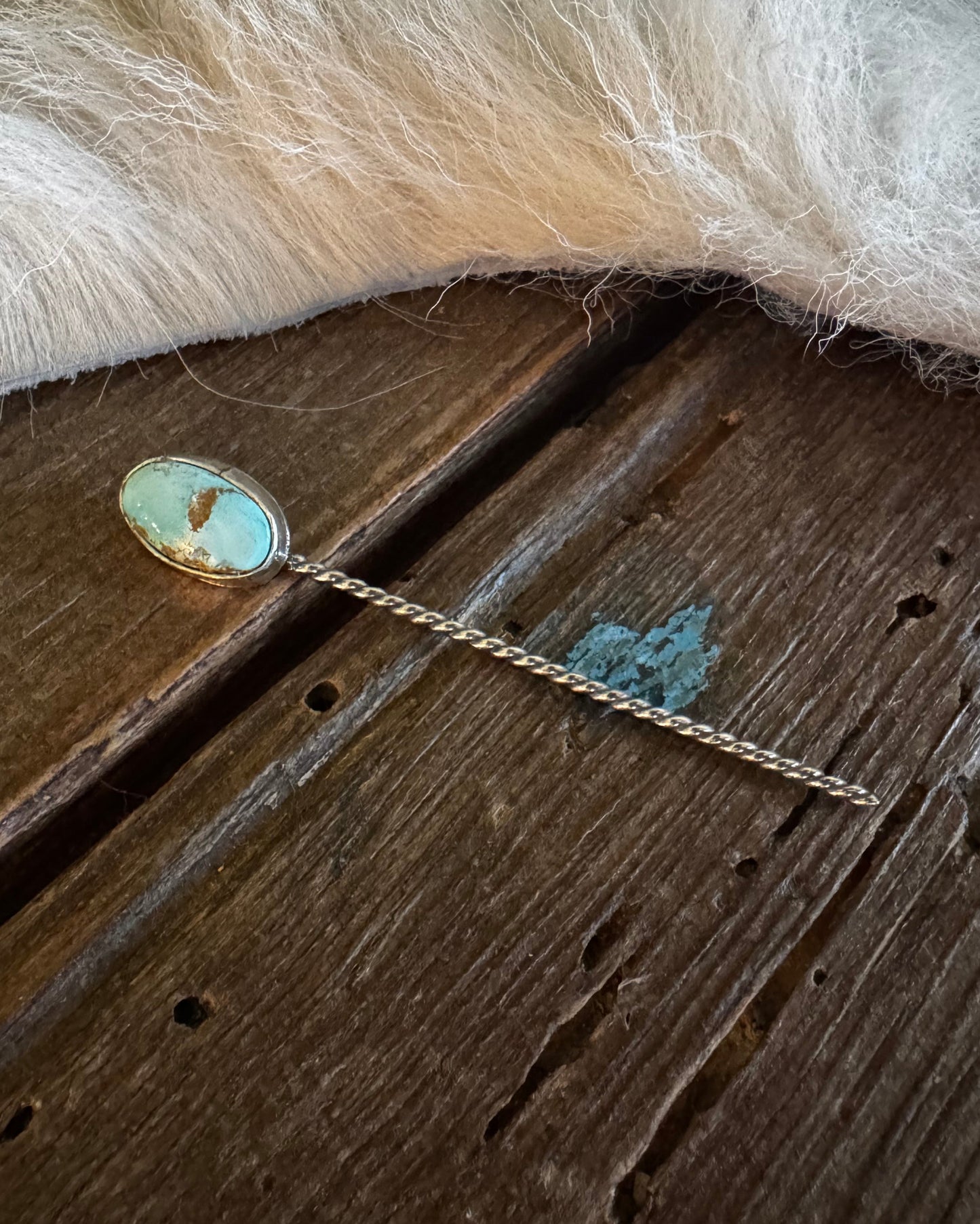 Teal stone hairpin on a wooden surface with fur