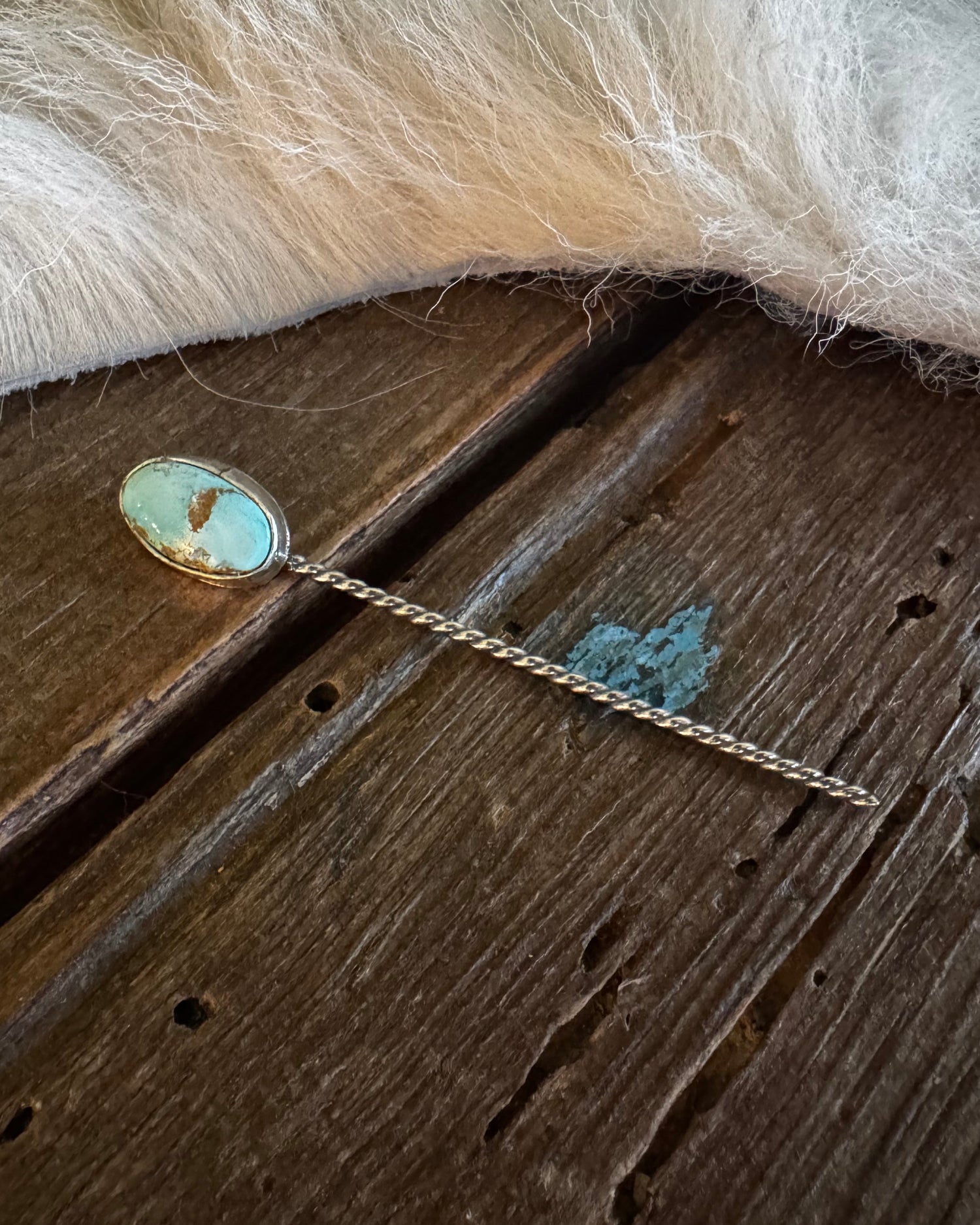 Teal stone hairpin on a wooden surface with fur